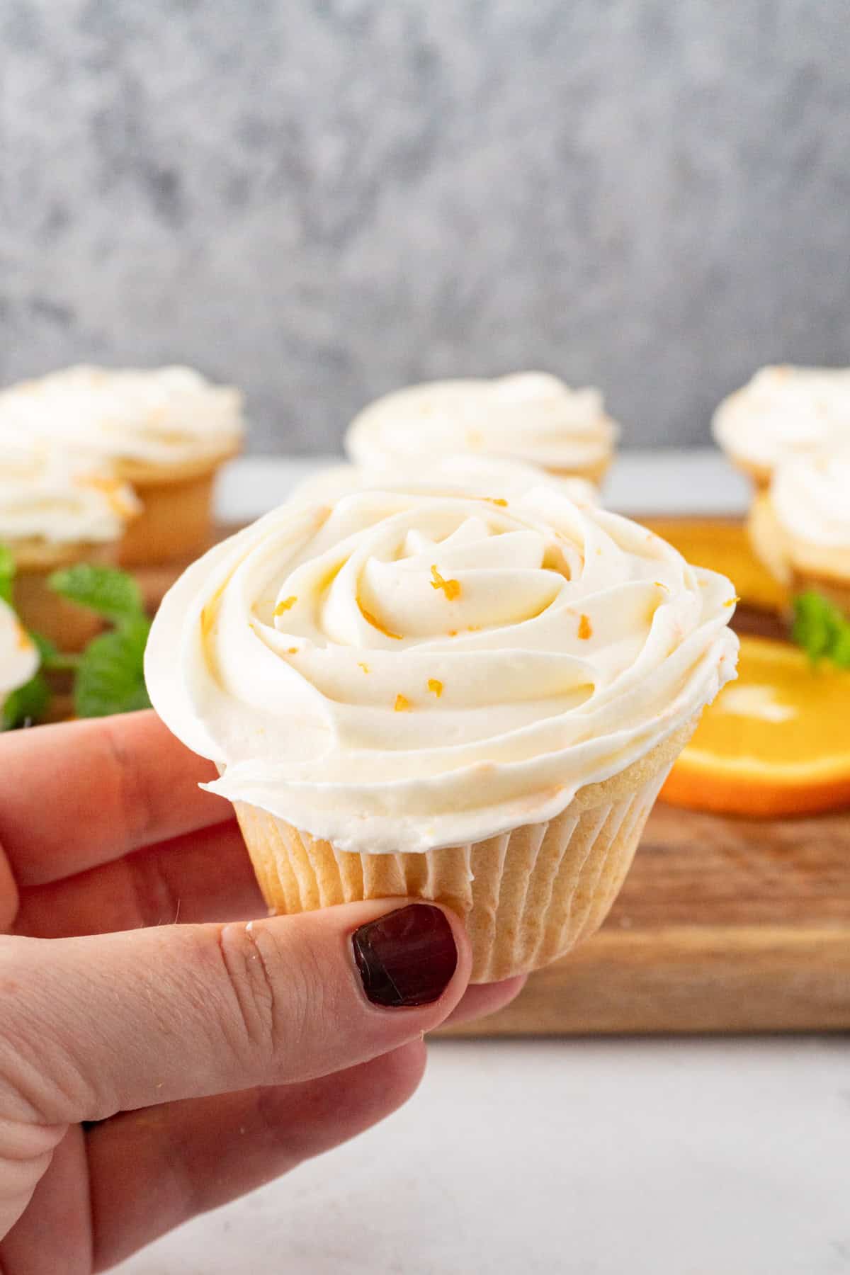 holding and orange cupcake frosted with cream cheese frosting.