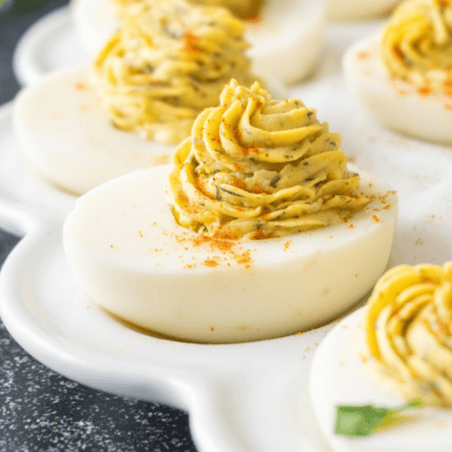 deviled egg on a white platter with piped filling into the white of the egg. featured image.