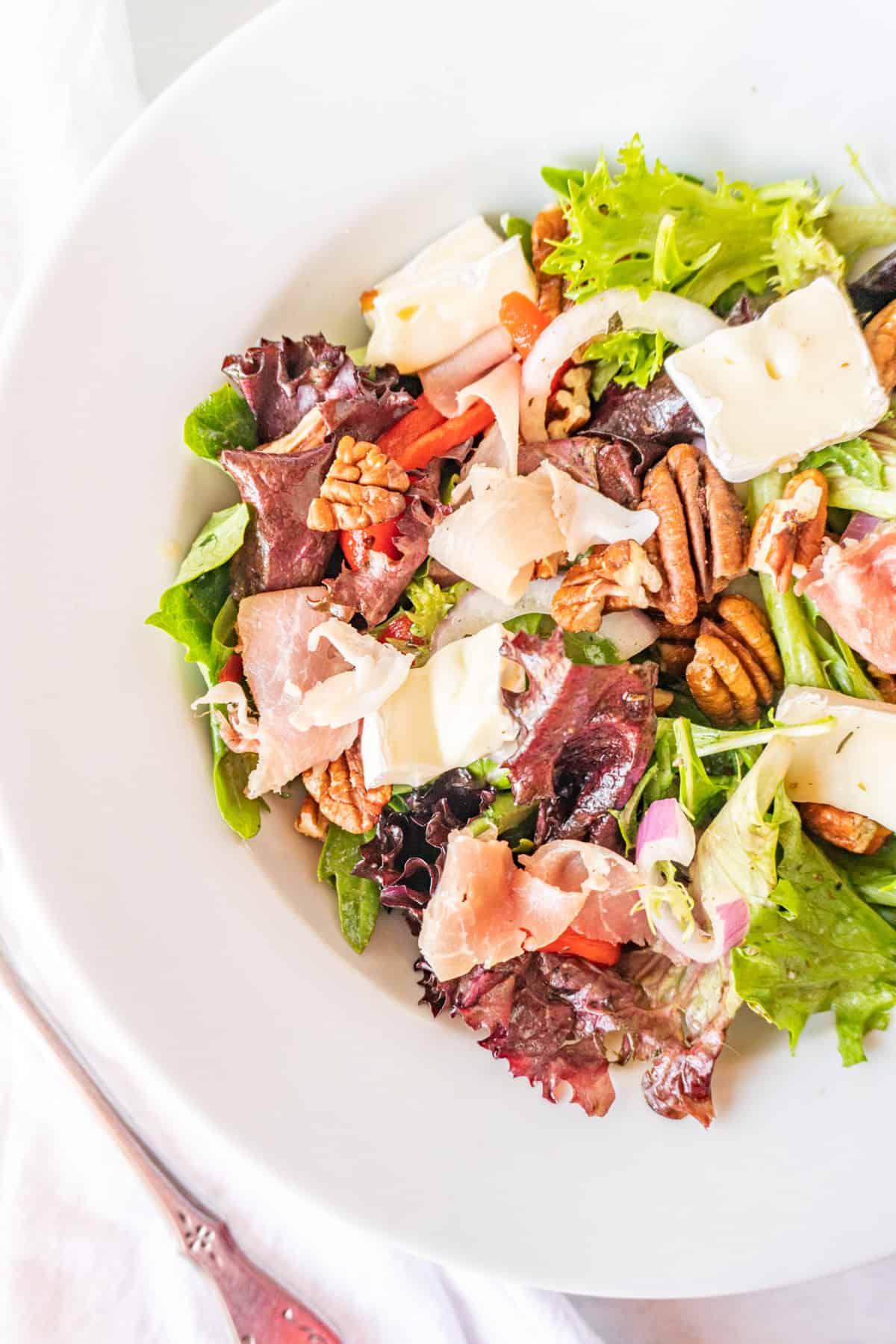 white salad bowl filled with salad mix, prosciutto, brie, red onion