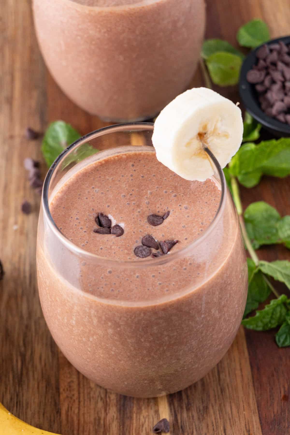 chocolate banana smoothie in glass with slice of banana and chocolate chips on top.