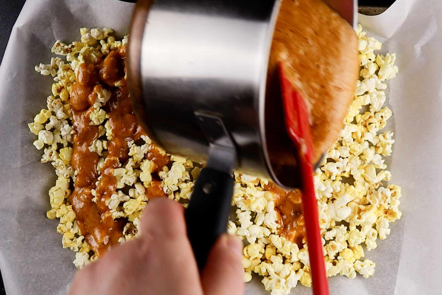 pouring caramel over popcorn on baking sheet