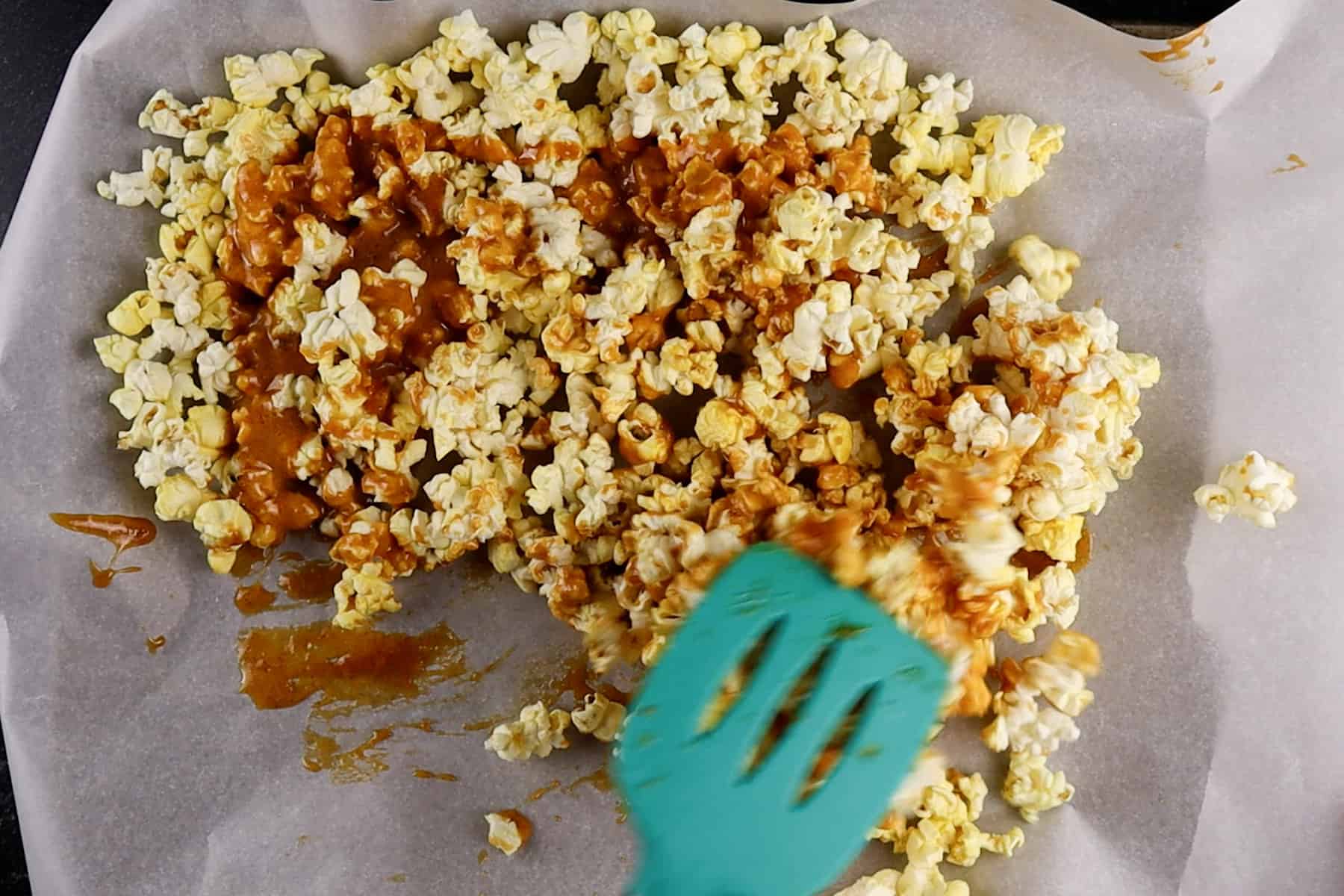 stirring popcorn on baking sheet