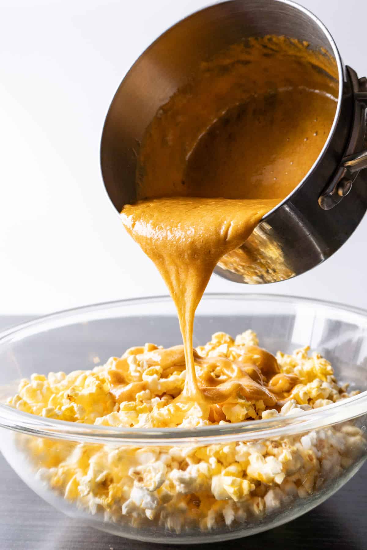 pouring caramel over popcorn in a bowl
