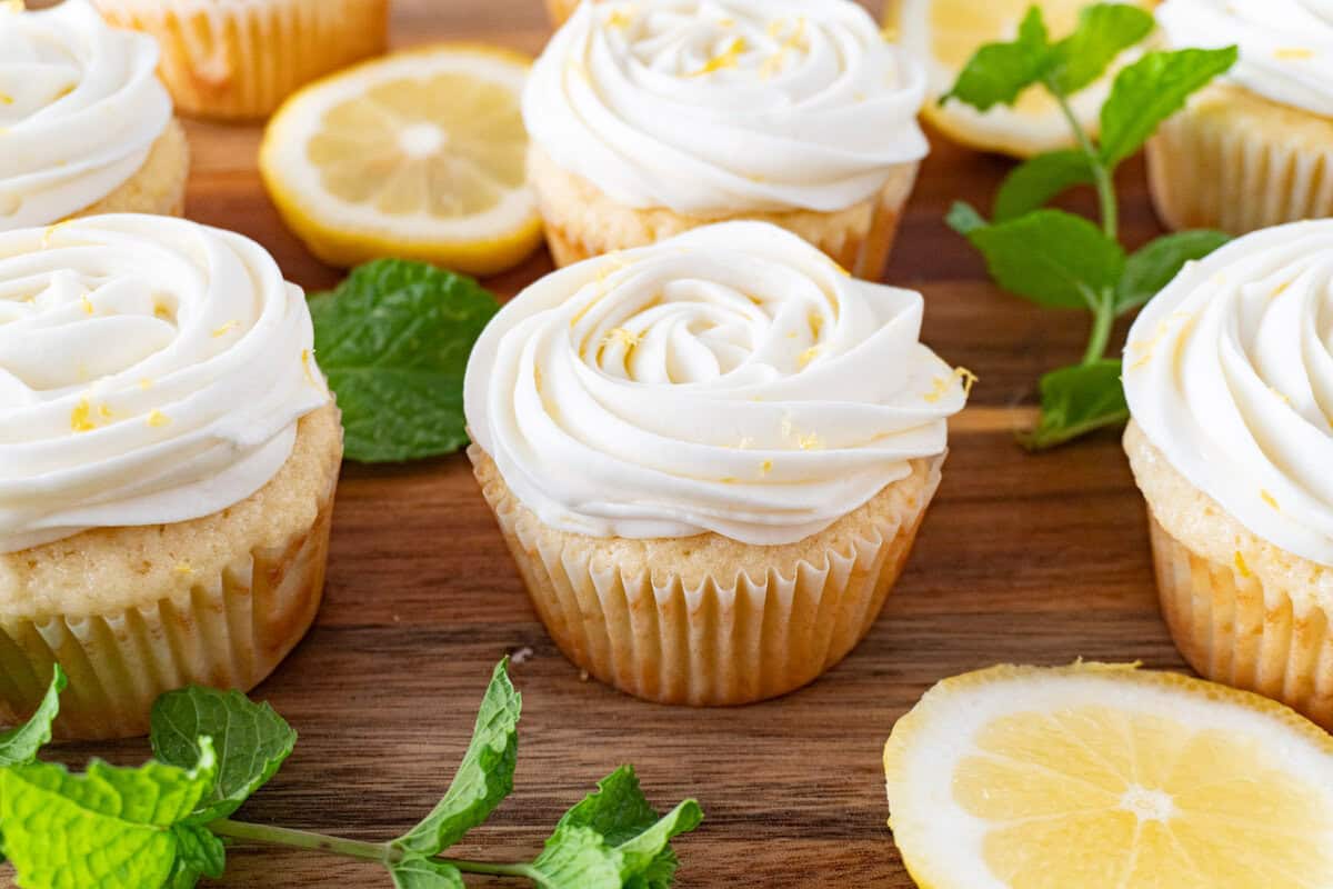 lemon cupcakes on cutting board with lemon slices and mint leaves as garnish.