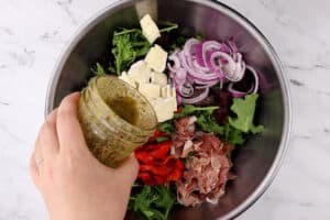 adding dressing to large bowl with salad ingredients