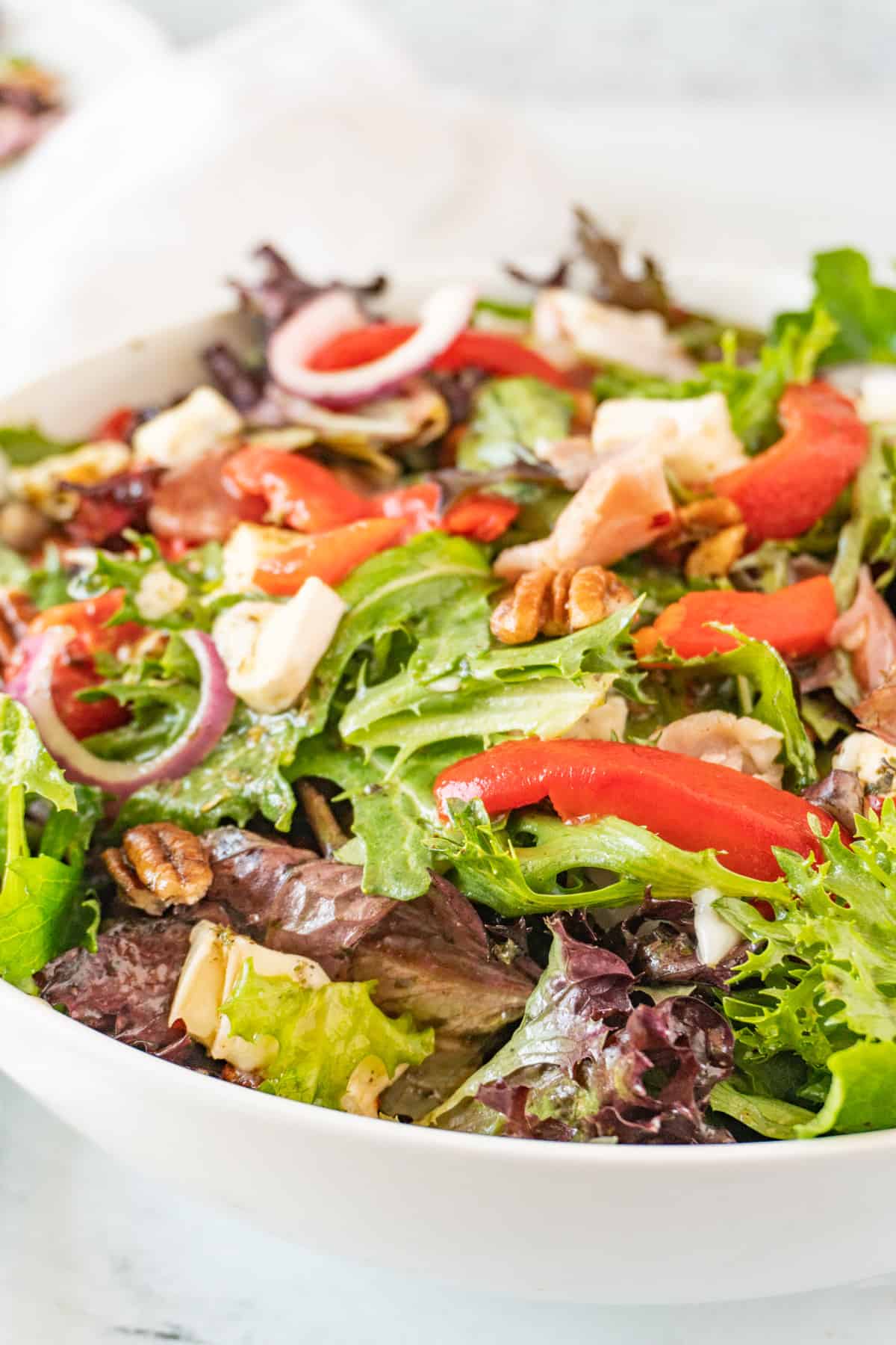 white salad bowl filled with salad mix, prosciutto, brie, red onion