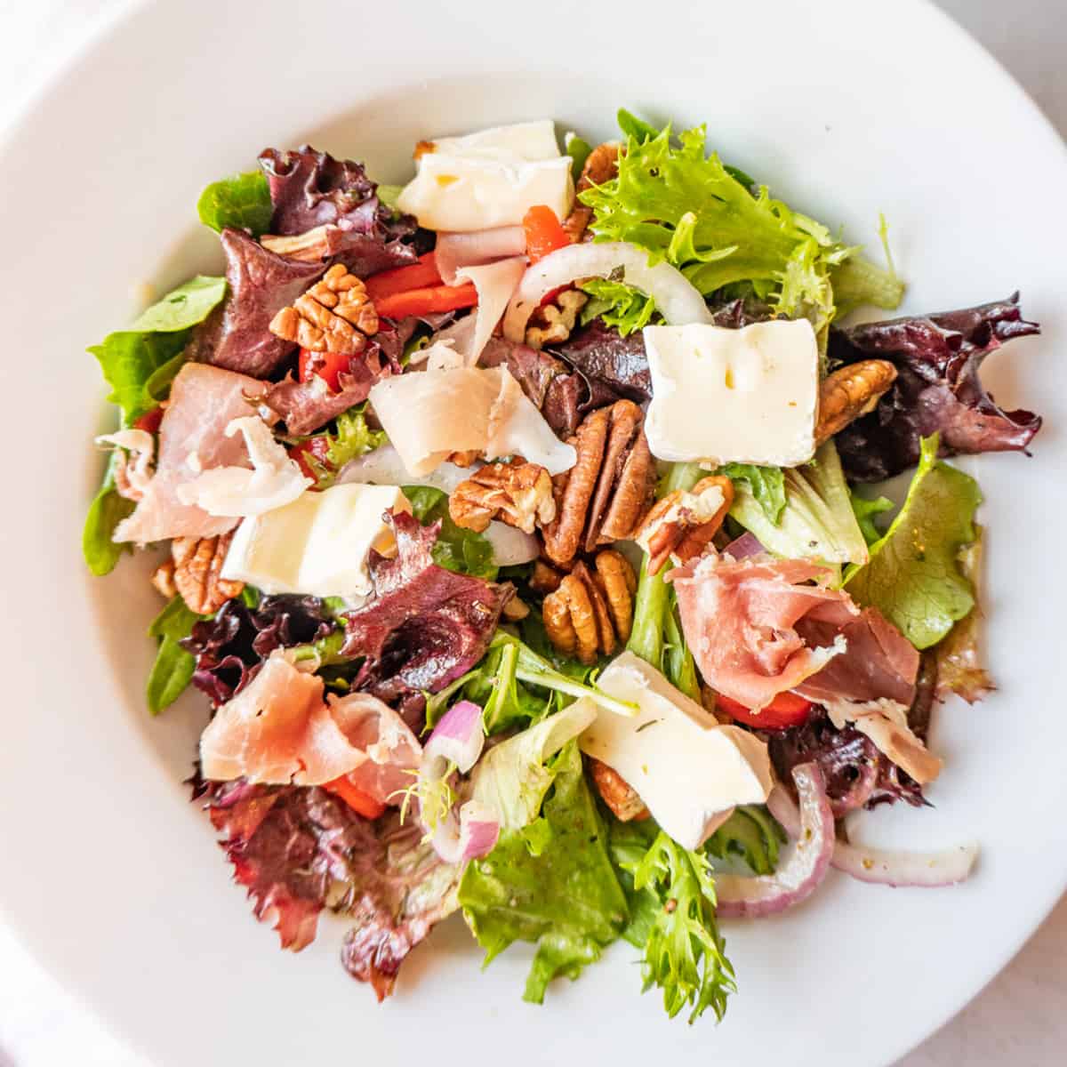 white salad bowl filled with salad mix, prosciutto, brie, red onion featured image