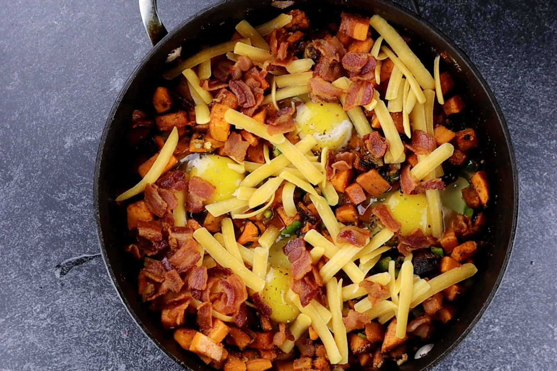 cheese and bacon sprinkled over skillet