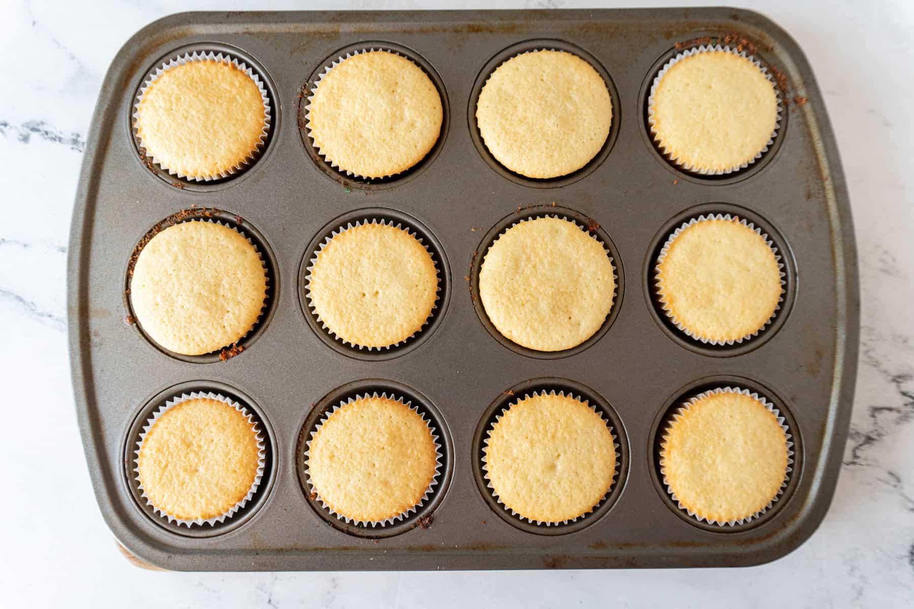 Baked yellow cupcakes in a cupcake tin.