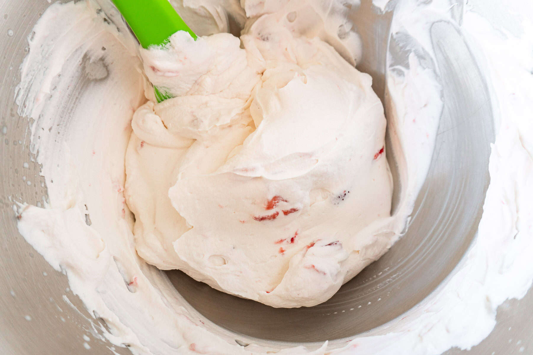 whipped cream berry frosting with berries folded in, in a metal bowl.