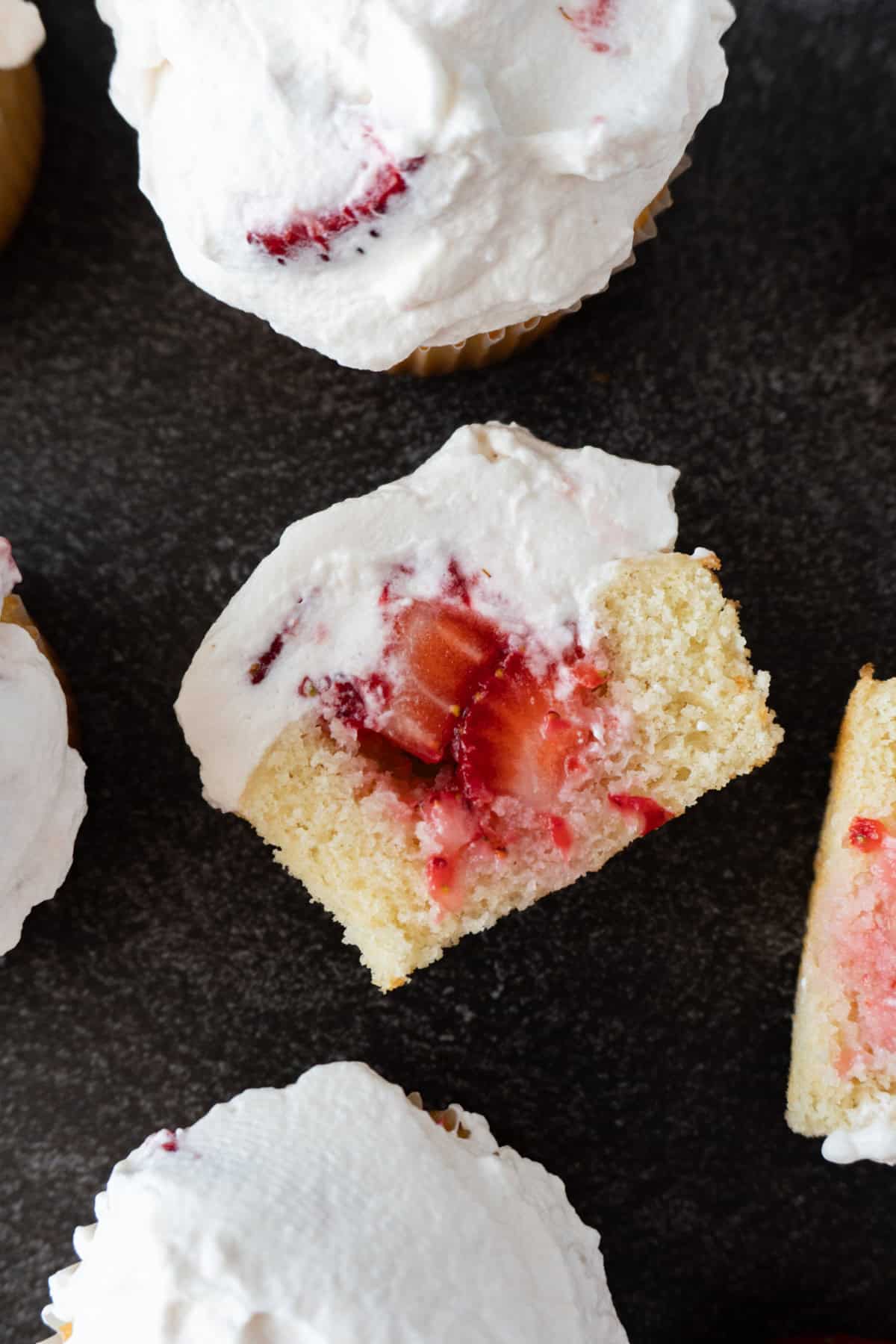 strawberry shortcake cupcake cut in half surrounded by uncut strawberry shortcake cupcake.