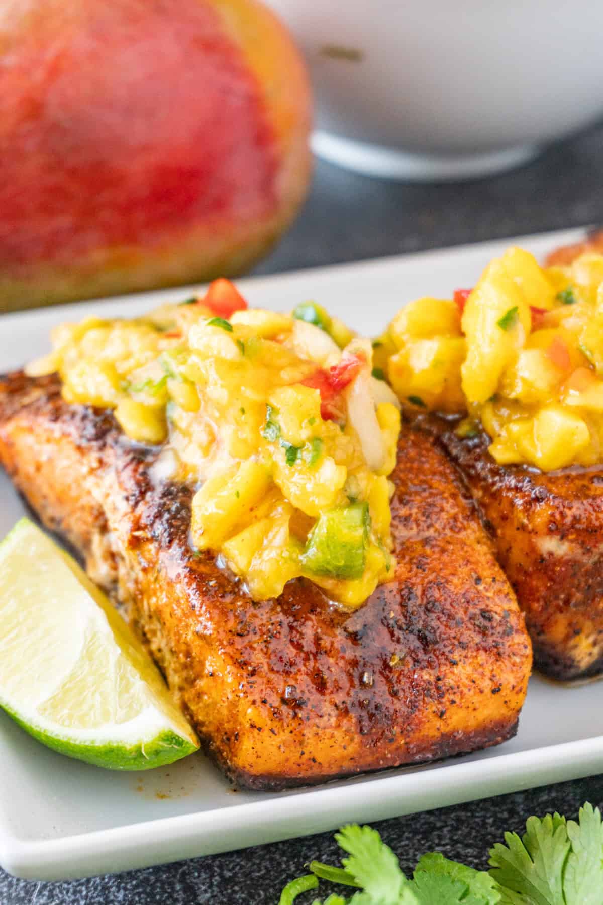 Salmon topped with Mango Salsa on a white plate, with lime wedges near the salmon.