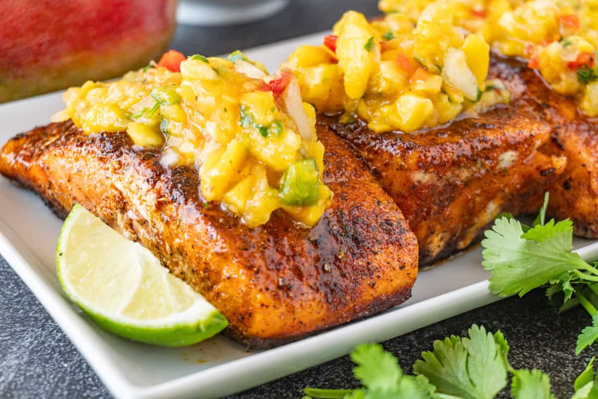 salmon filets on a white plate with lime wedge and topped with mango salsa.