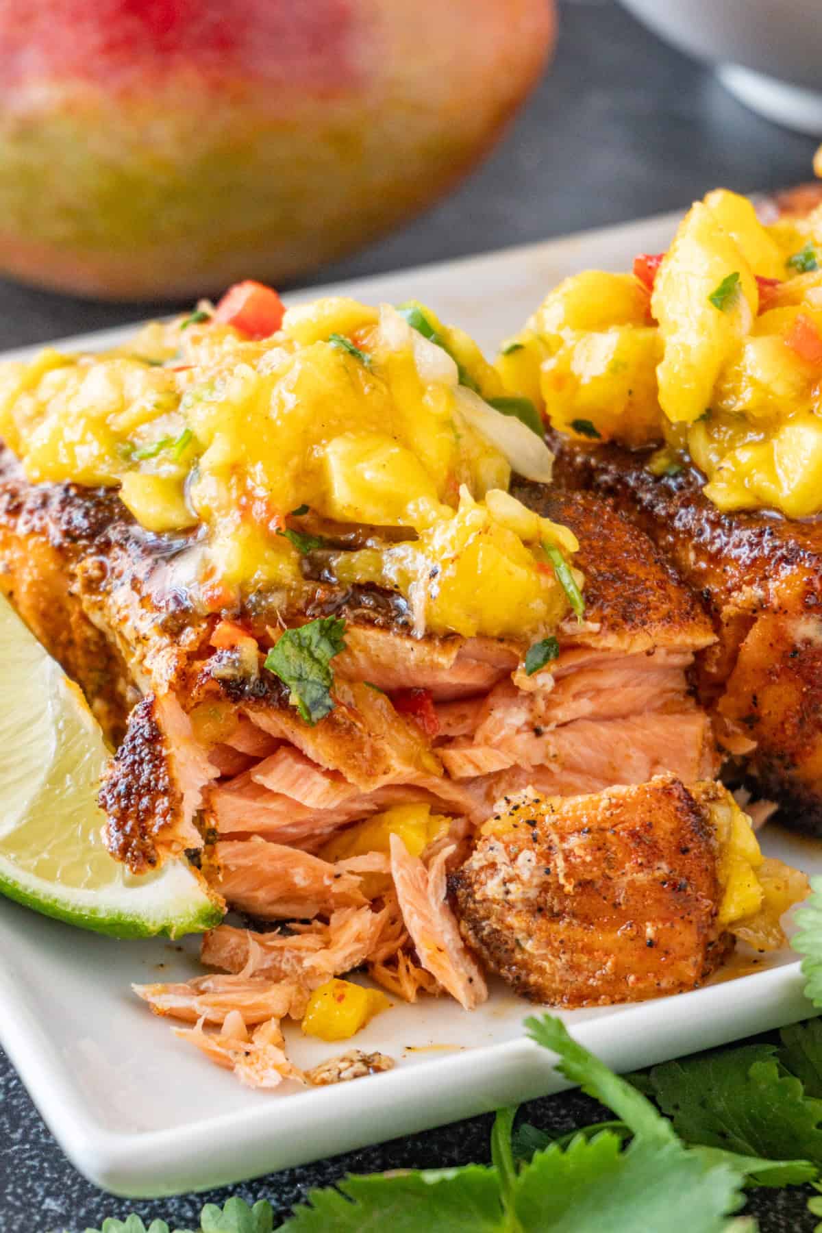 Salmon cut open to show cooked flaky layers, topped with mango salsa, sitting on a white plate.