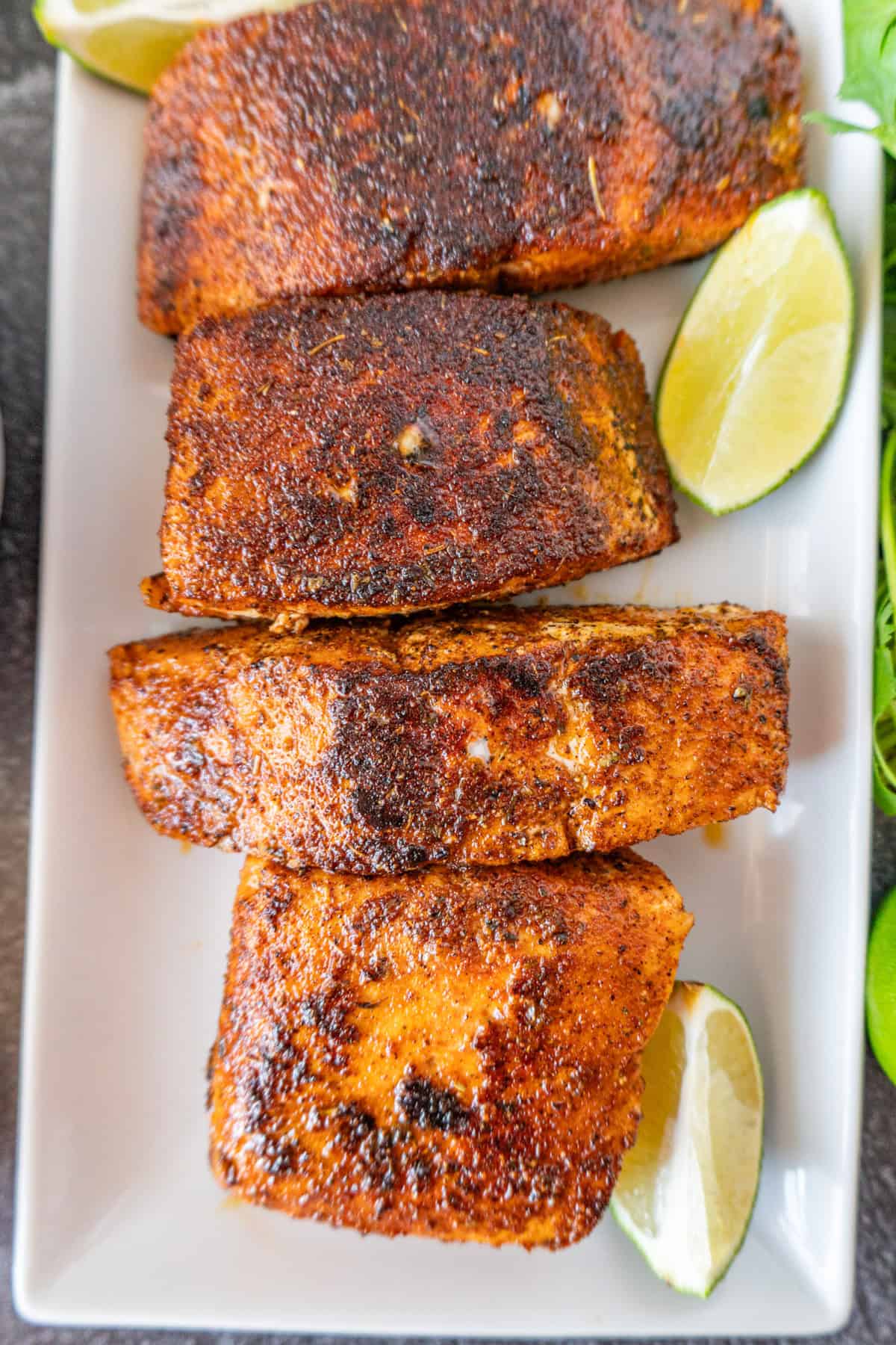 cooked salmon on a white platter with lime wedges nearby.