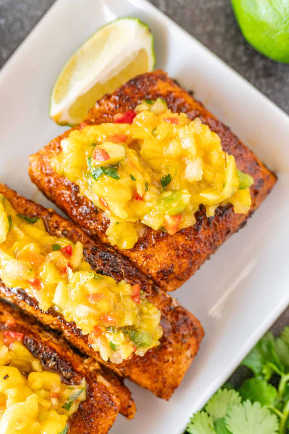 Salmon topped with Mango Salsa on white plate, with lime wedges near salmon.