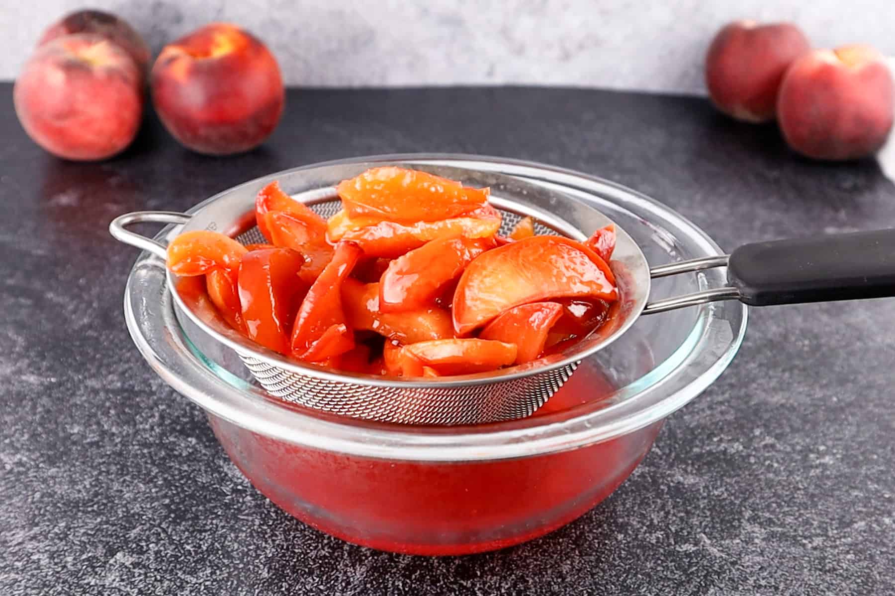 strainer with peaches in it and syrup in bowl beneath