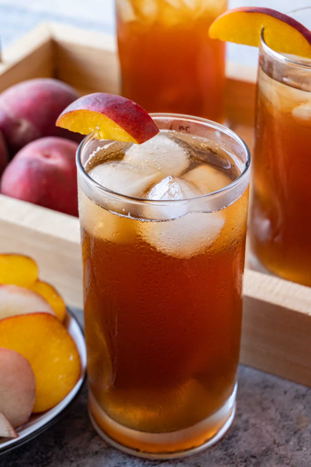 peach tea in glass with ice cubes and peaches in background