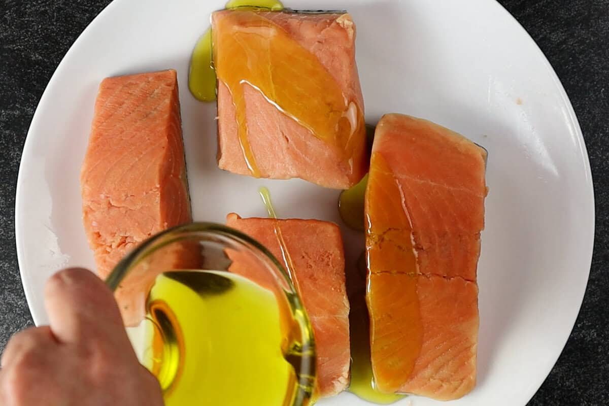 coating salmon in olive oil on white plate.
