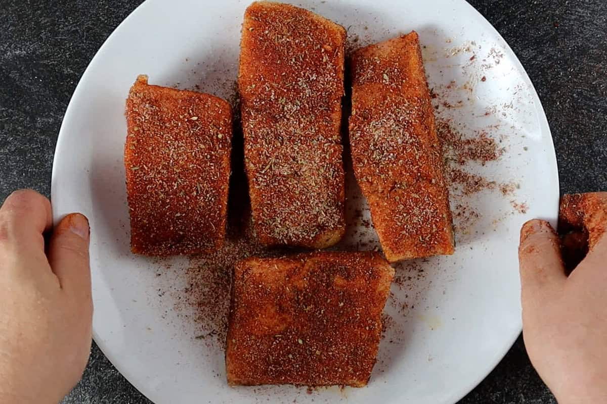 salmon filets coated with dry rub on white plate.