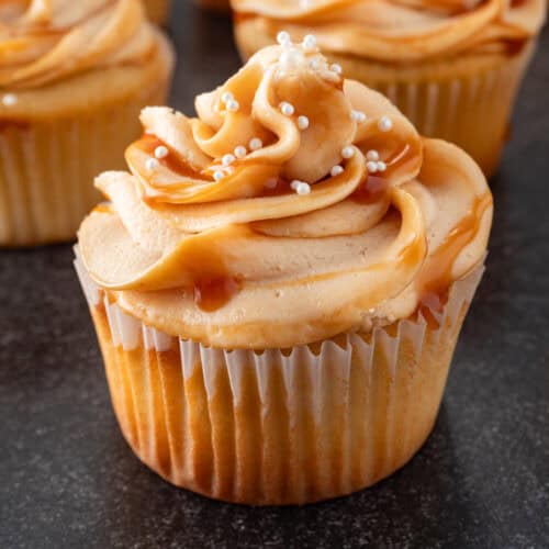 caramel frosting piped on cupcake with white sprinkles featured image.