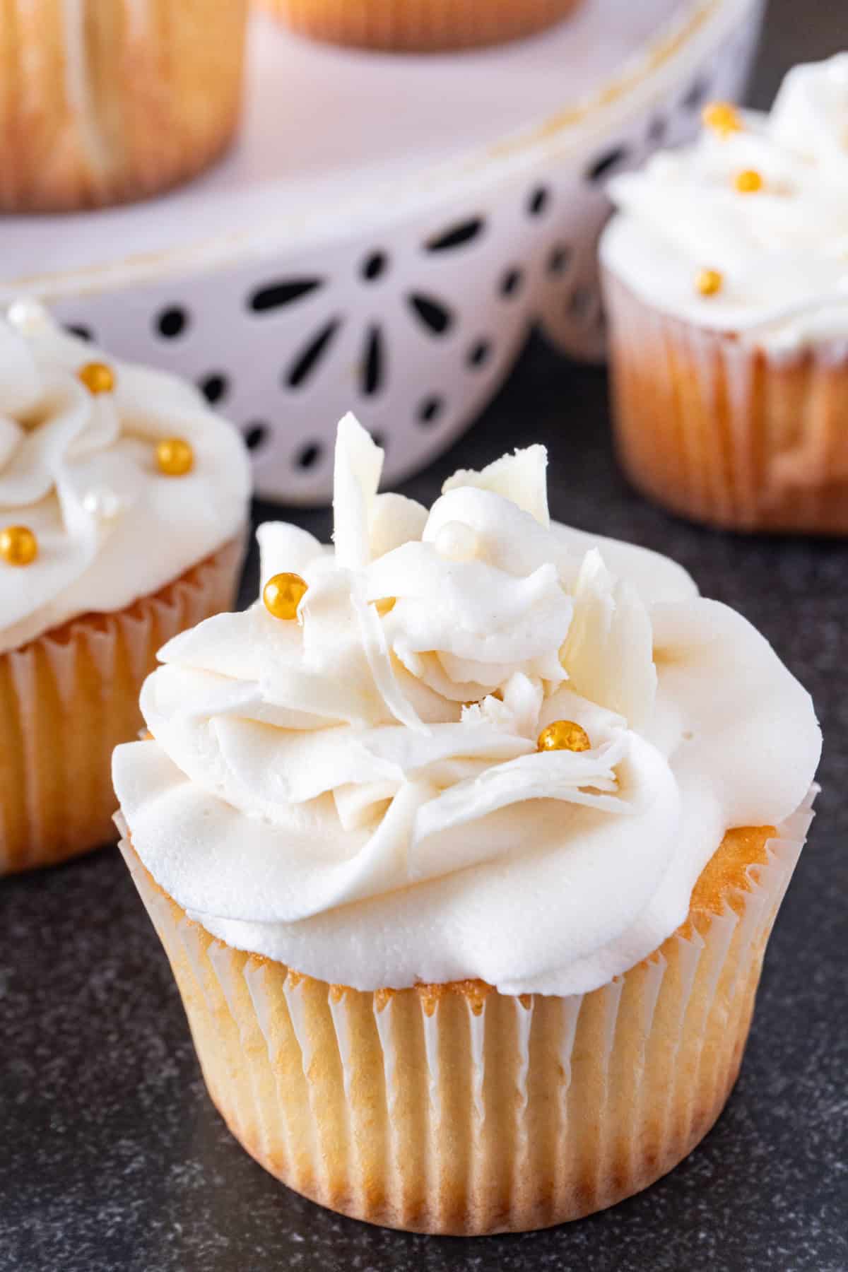White chocolate cupcakes with white chocolate frosting and gold and white sprinkles, and pieces of white chocolate.