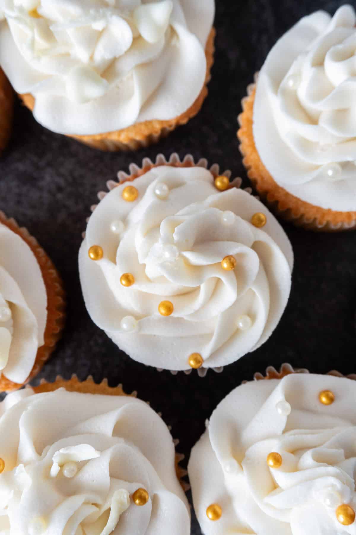 Beautiful swirl of frosting topped with gold and white sprinkles on cupcake.