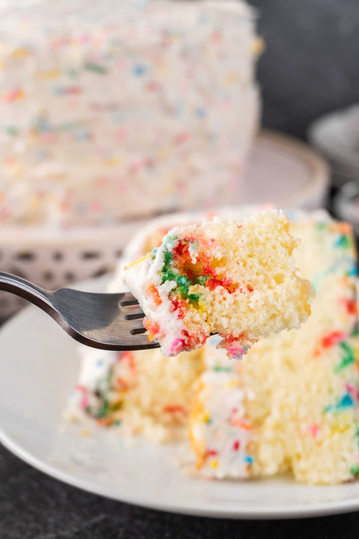 Birthday cake on a fork with cake in the background.