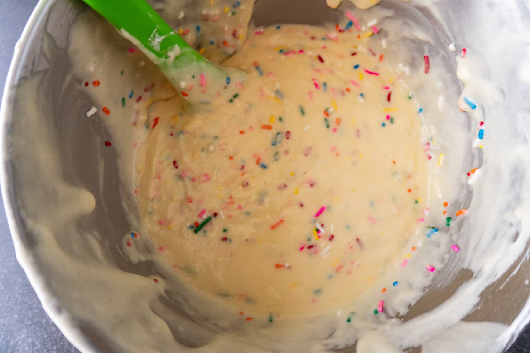 Cake batter with sprinkles folded in, in a metal mixing bowl.