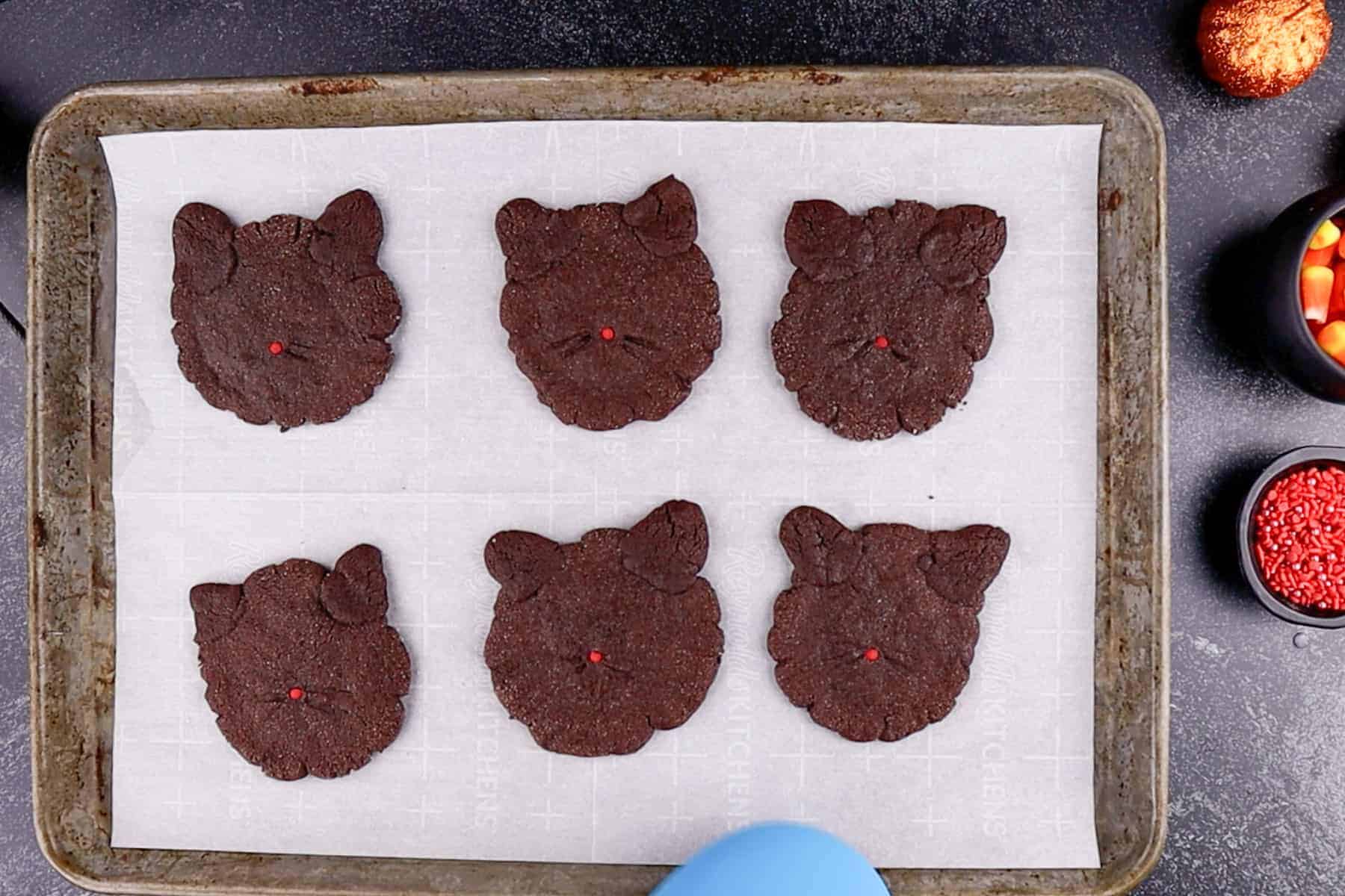 Baked black cat cookies on parchment-lined cookie tray.