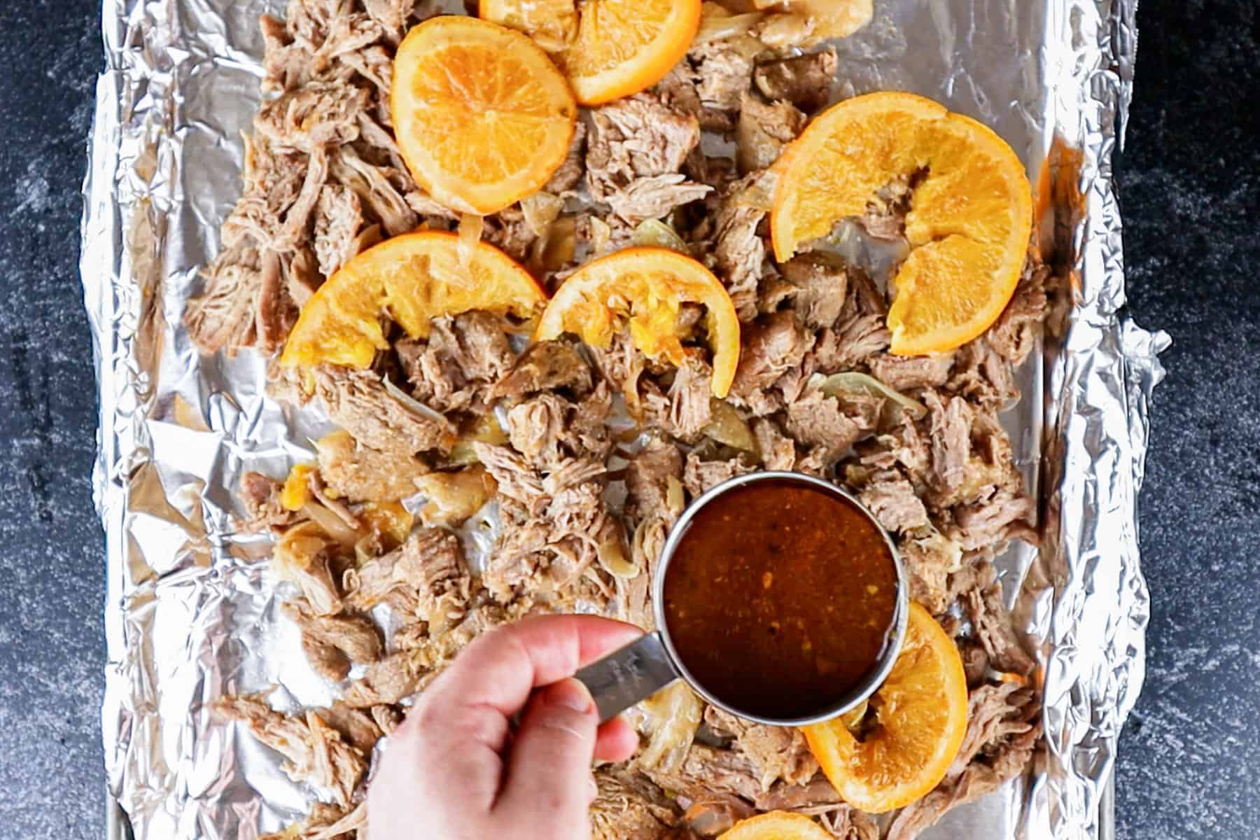 Pouring broth over shredded pork on foiled lined baking sheet.