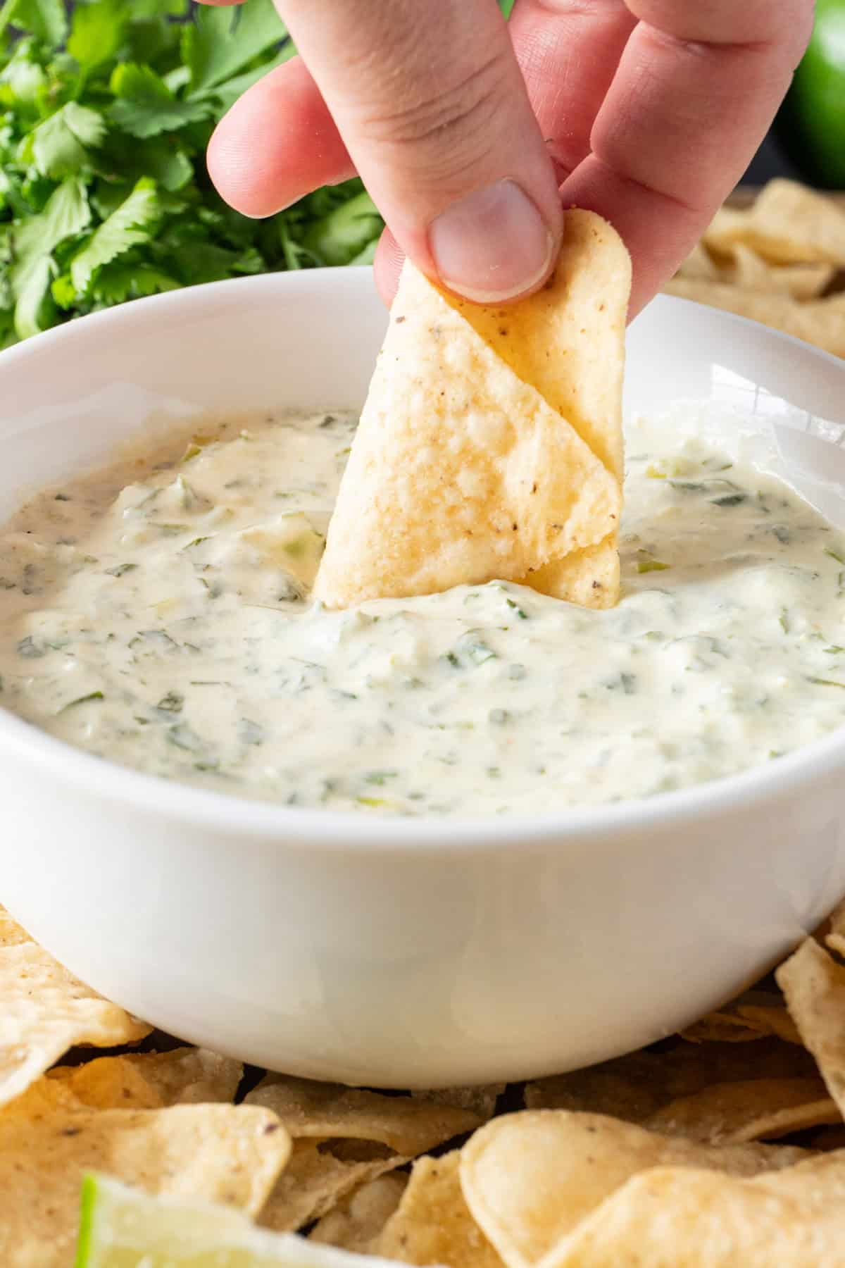dipping a chip in cilantro lime sauce in white bowl