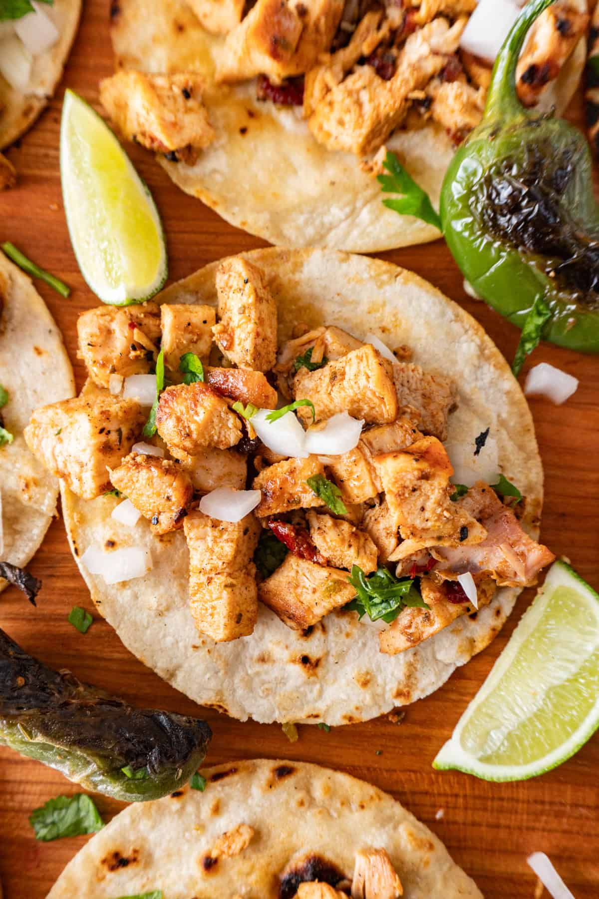 chicken street taco with lime wedges and charred jalapeno around it.