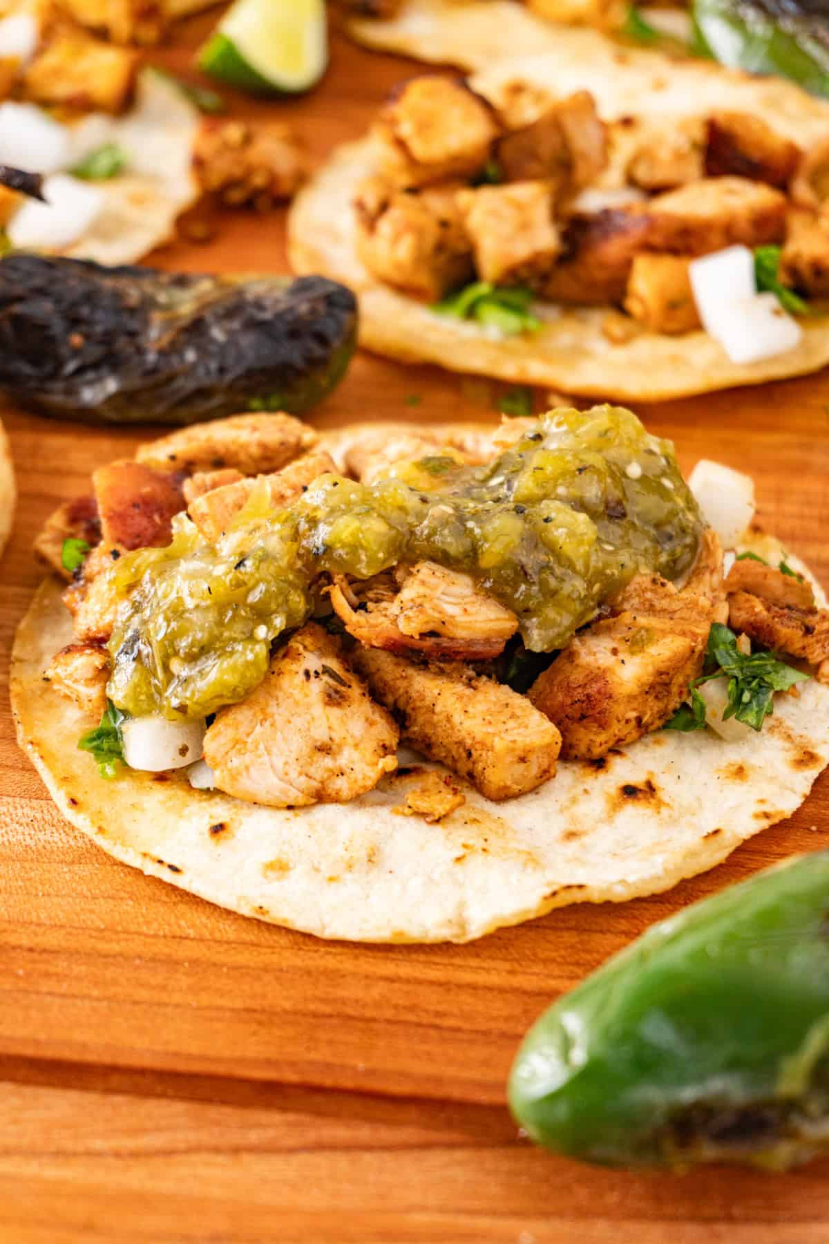 chicken street tacos with tomatillo salsa on top, sitting on wooden cutting board.