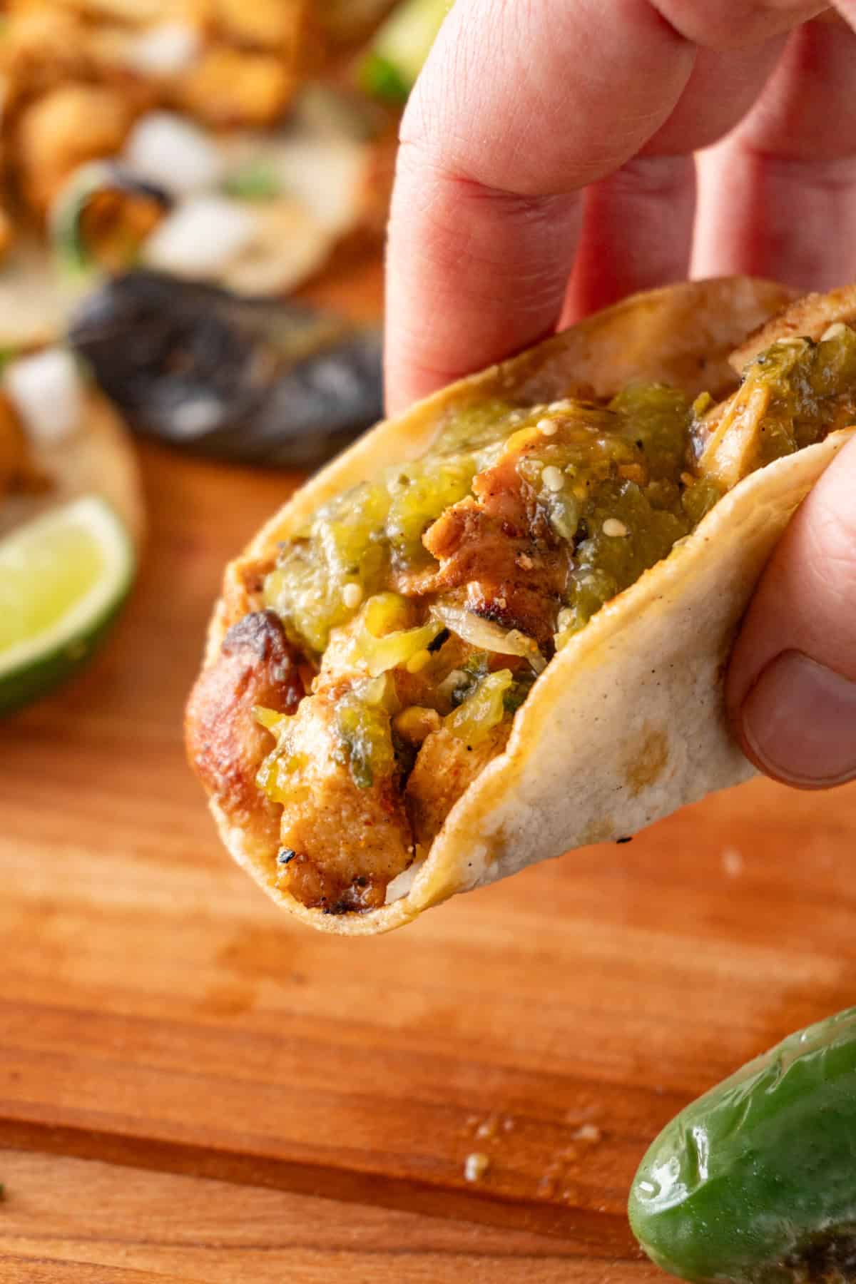 holding a chicken street taco topped with tomatillo salsa.