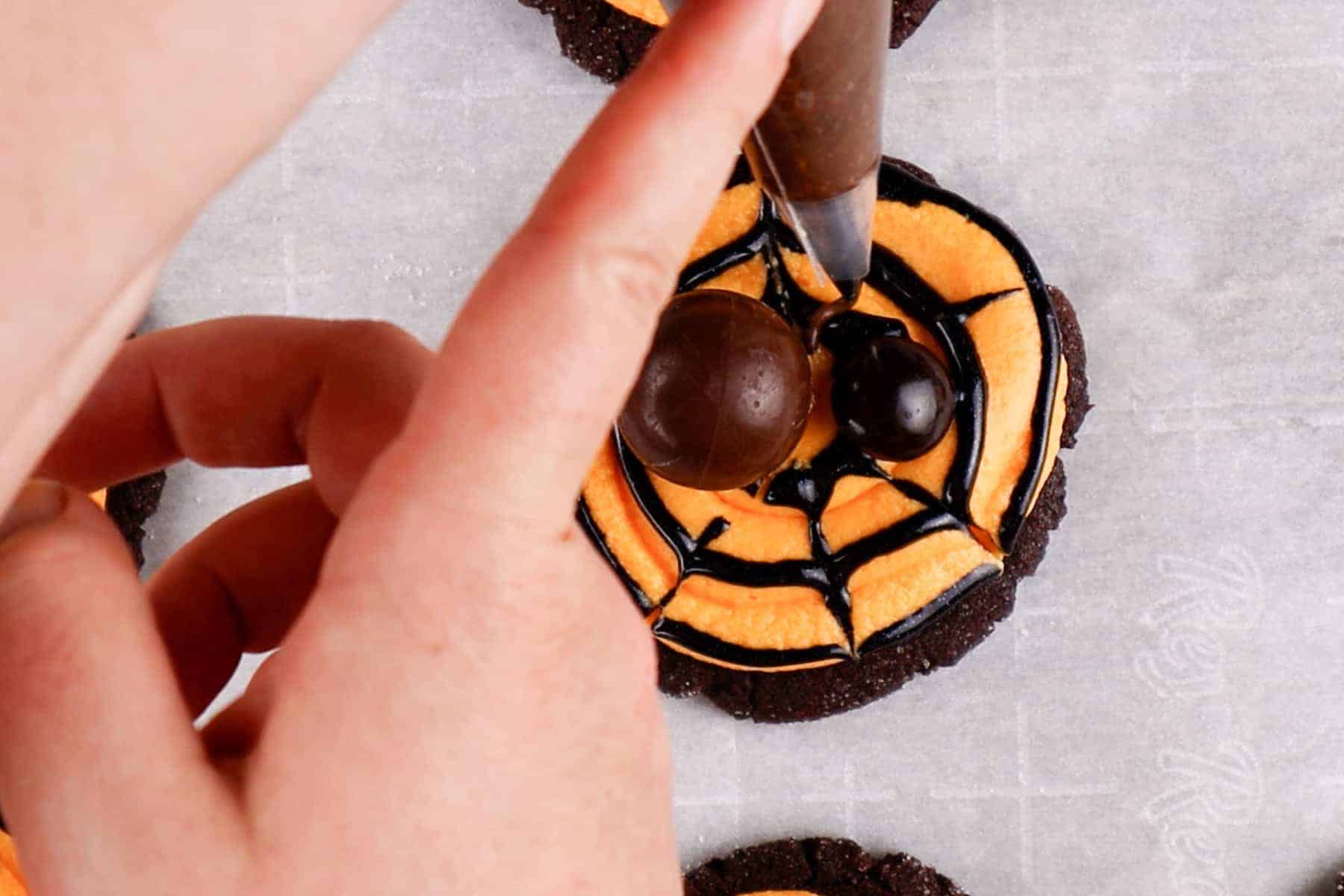 Using chocolate frosting to pipe on legs to the spider.