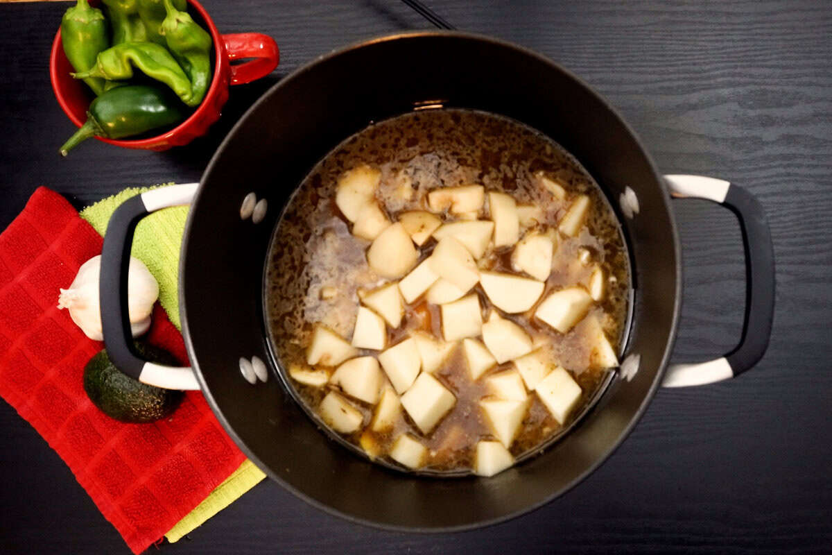 potatoes added to stew pot. Fresh green chiles in red cup near pot.