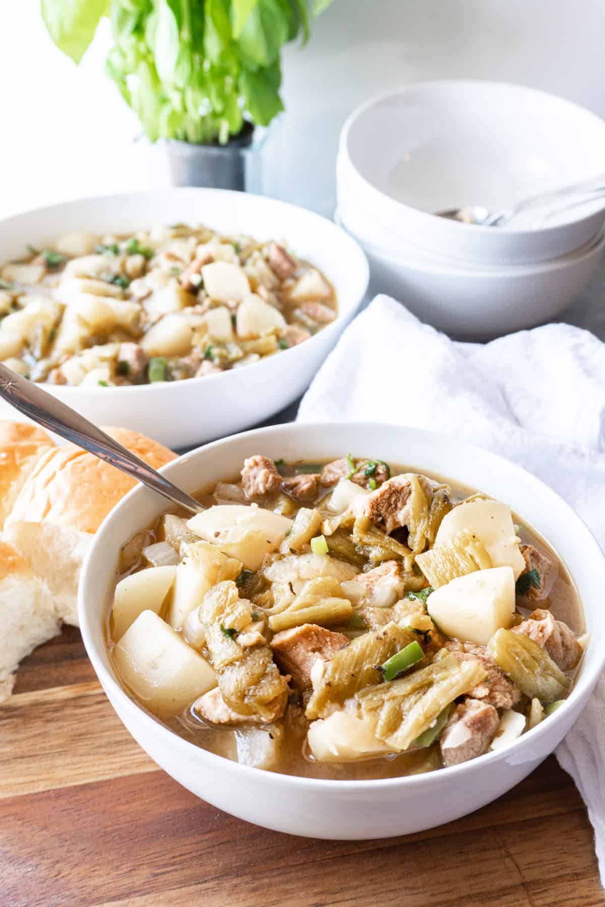 green chile stew in white bowls sitting on a wooden cutting board.