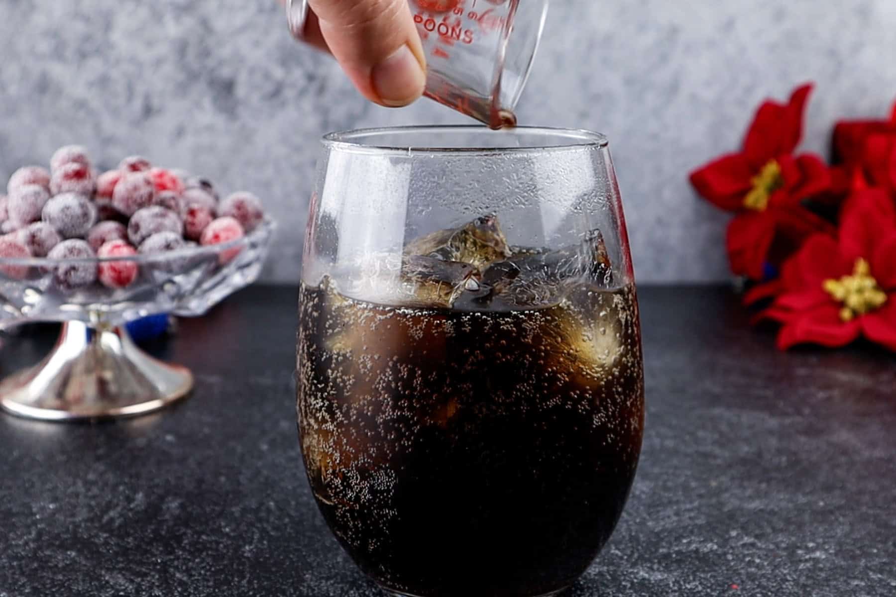 Frosted glass of soda with ice cubes, pouring vanilla into glass, festive holiday setting.
