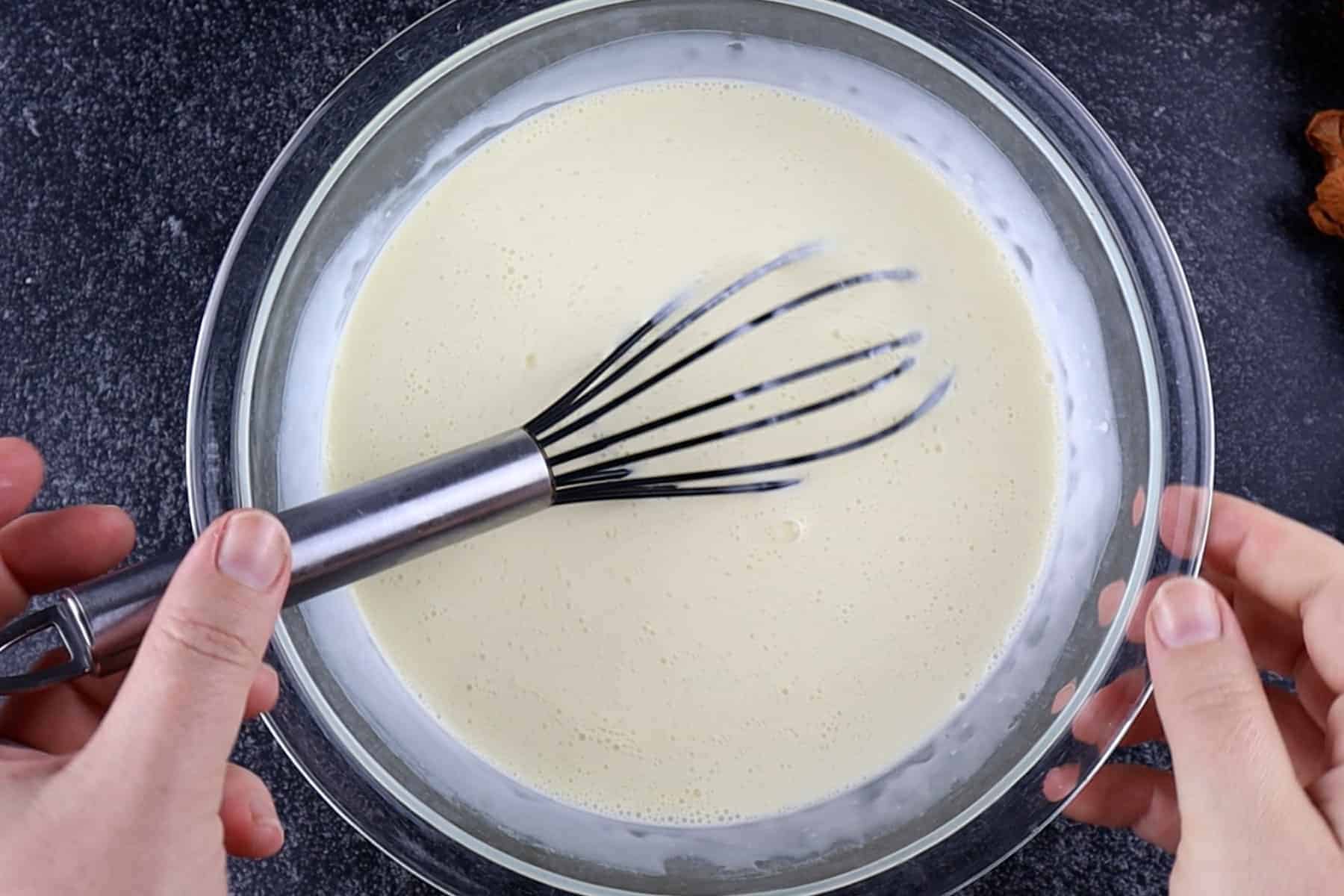 Whisked egg, milk, and cream mixture in a glass bowl.