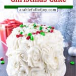 Holiday Cake Pinterest Pin, cake decorated with white frosted rose swirls, M&Ms, and sprinkles, Christmas decorations in the background.