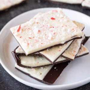 Peppermint bark stacked on a white plate with more peppermint bark in the background.