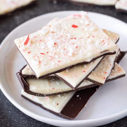 Peppermint bark stacked on a white plate with more peppermint bark in the background.