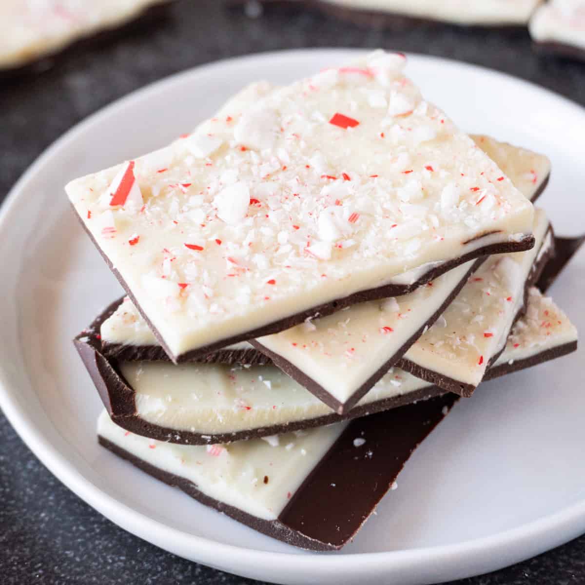 Peppermint bark stacked on a white plate with more peppermint bark in the background.