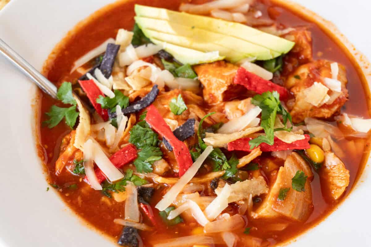 chicken tortilla soup in white bowl garnished with avocado, chips, green onions