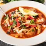 chicken tortilla soup in white bowl garnished with avocado, chips, green onions, featured image.