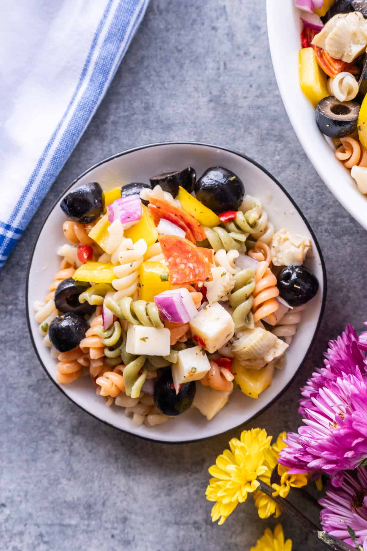 pepperoni pasta salad on plate next to napkin and flowers