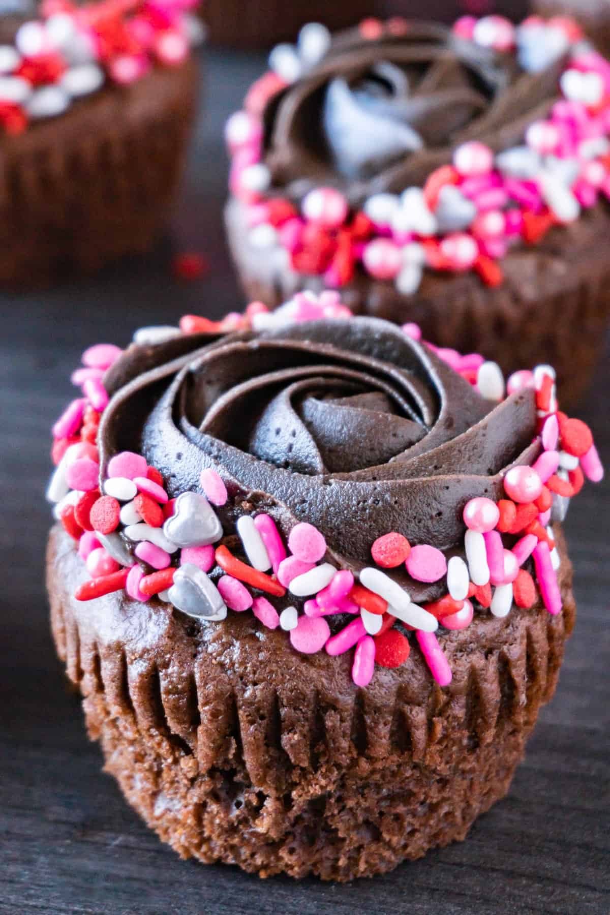 Valentine's Day Cupcakes- an easy treat for your sweetheart! Dark chocolate cupcakes, with dark chocolate frosting, fun Valentine sprinkles, and a lindor truffle center! valentine's day cupcake close up