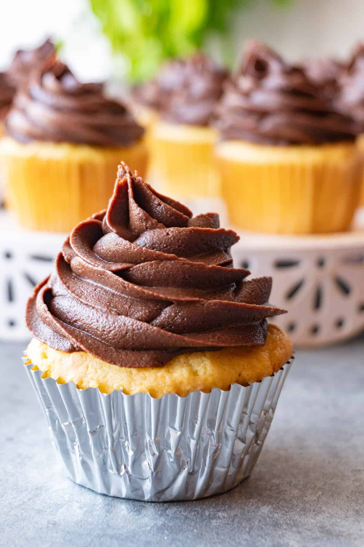 chocolate fudge frosting piped into a high swirl onto a yellow cupcake.