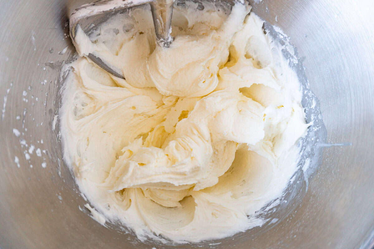 butter, powdered sugar, and heavy cream mixed in a metal bowl.